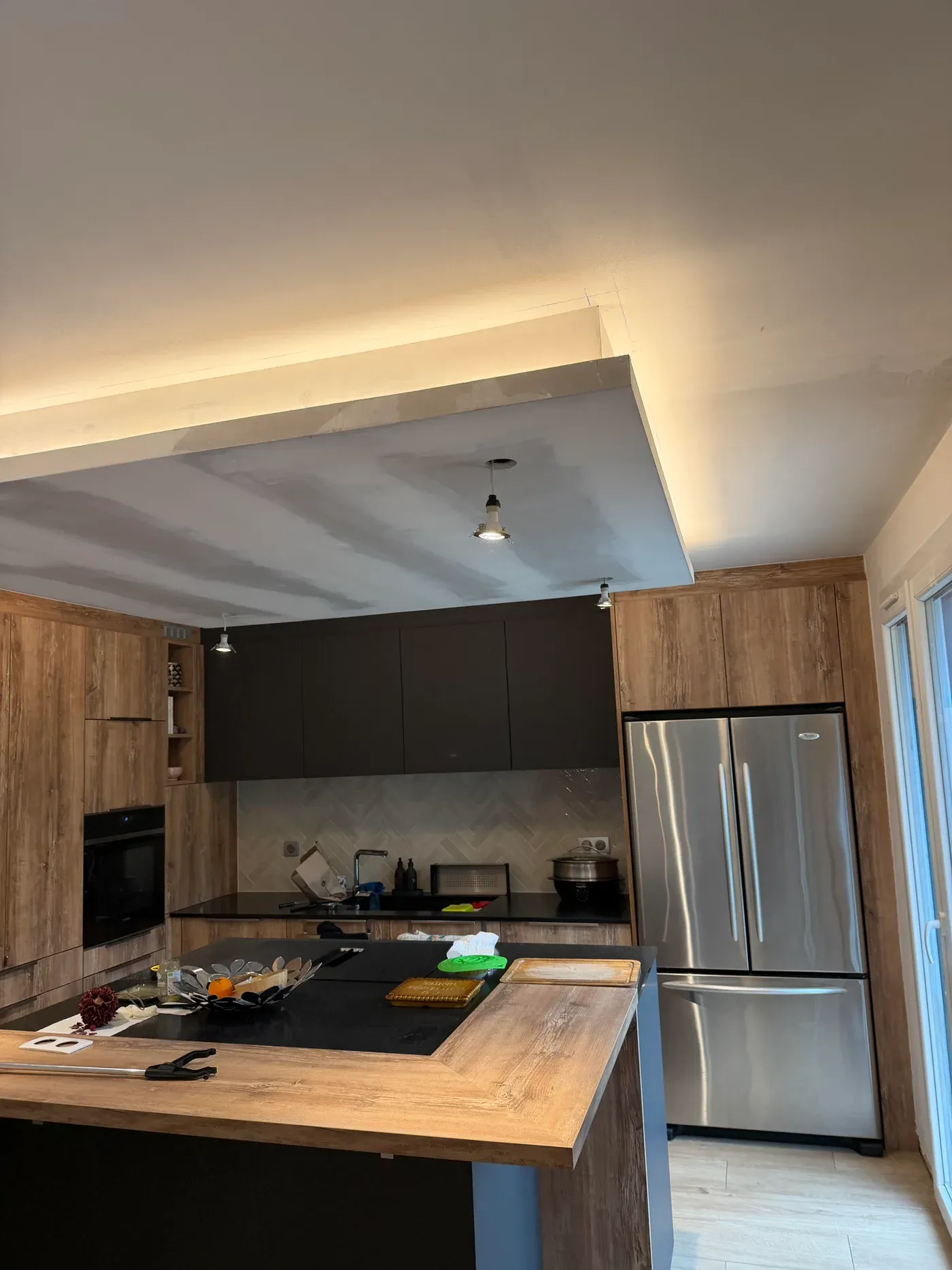 Cuisine équipée terminée — îlot, plan de travail bois, faux-plafond LED